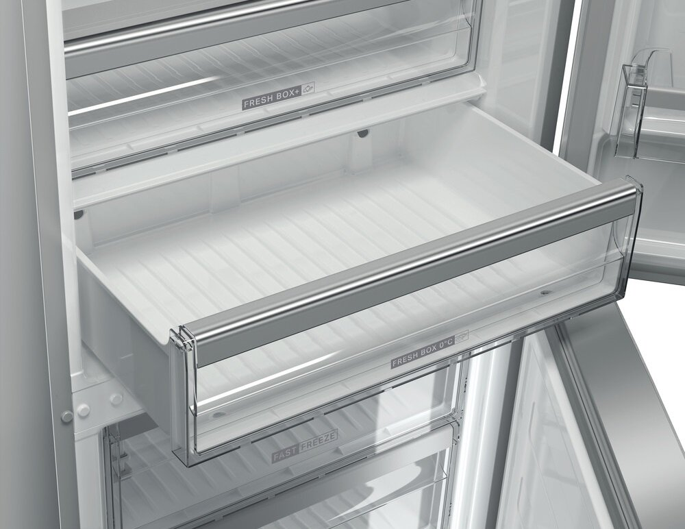 Zbliżenie na szufladę lodówki, pokazujące przezroczyste pojemniki i metalowe wykończenia.