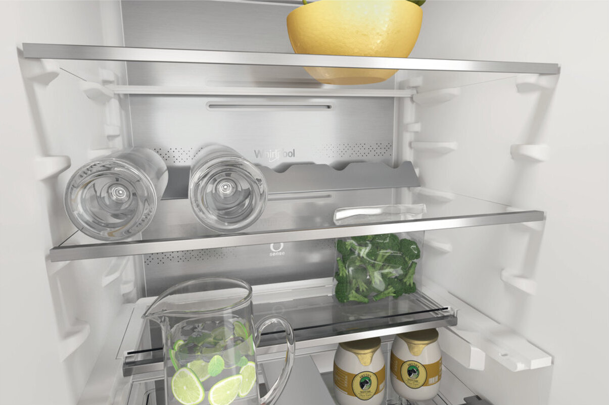 Wnętrze lodówki. Słoik z cytrynami, butelki z wodą i miska z zielenią.