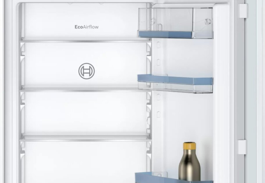 Wnętrze lodówki pokazujące półki i butelkę z płynem. Białe wnętrze.