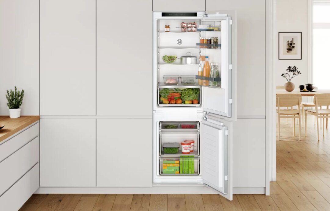 Biała kuchnia z otwartą lodówką, półki wypełnione.