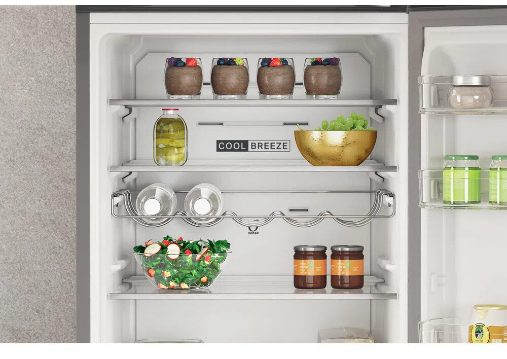 Widok wewnętrzny lodówki ze szklanymi słoikami, świeżą żywnością i miską winogron na półkach.