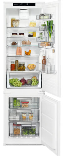 Biała lodówka z otwartymi drzwiami, ujawniająca półki z żywnością i szuflady, różne pojemniki.