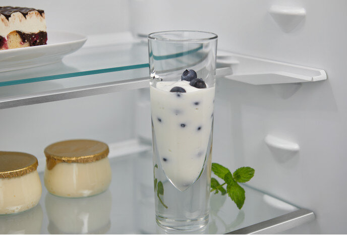 Zbliżenie na szklankę z jogurtem i borówkami na półce, z miętą i deserami.