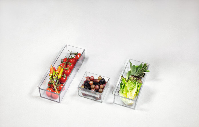 Trzy przezroczyste prostokątne pojemniki ze świeżymi produktami, ułożone na białej powierzchni.