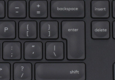 Zbliżenie ciemnoszarej klawiatury z podświetlonym klawiszem Enter i widocznymi innymi klawiszami.