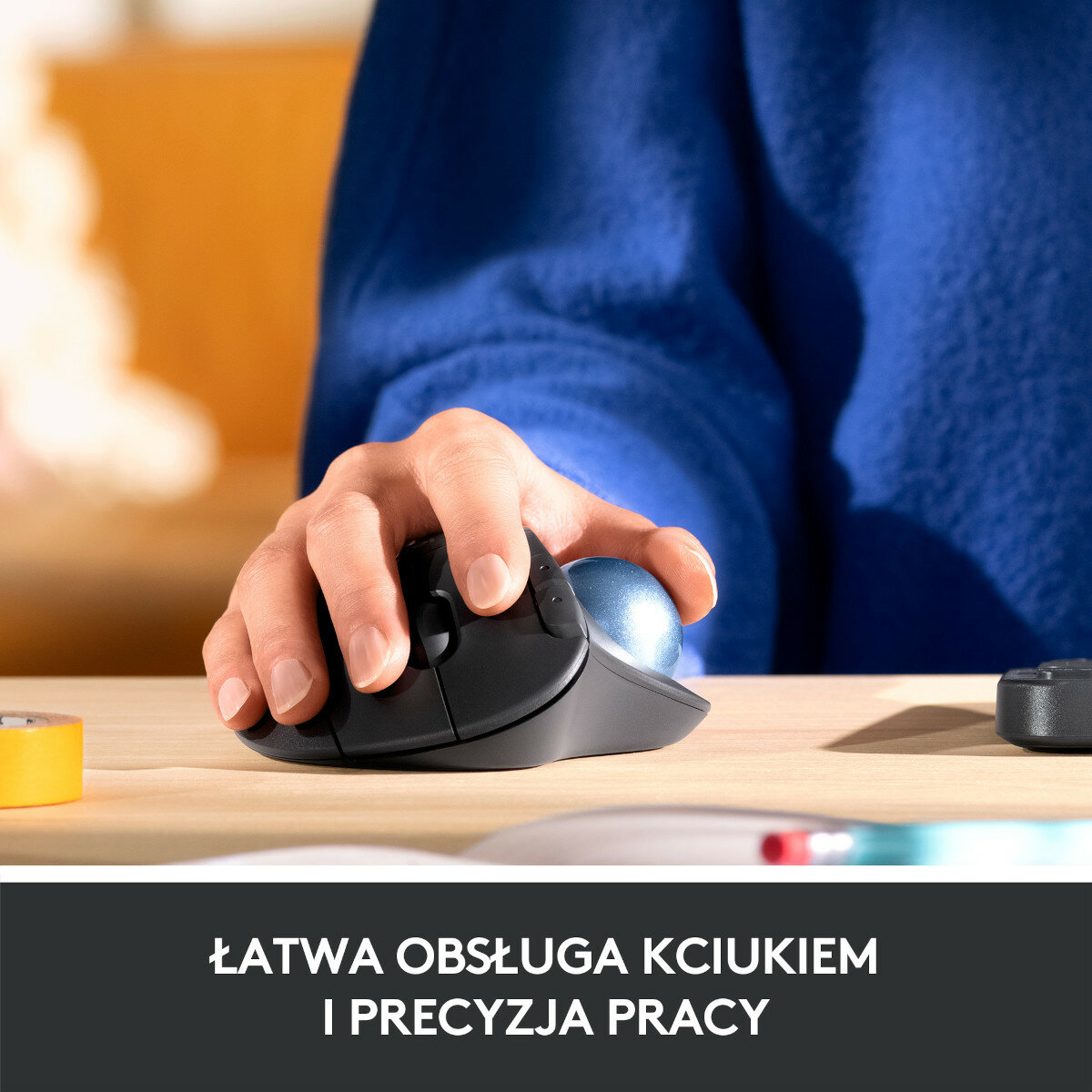 Dłoń osoby używającej myszy trackball. Mysz jest czarna i ma niebieską kulkę.