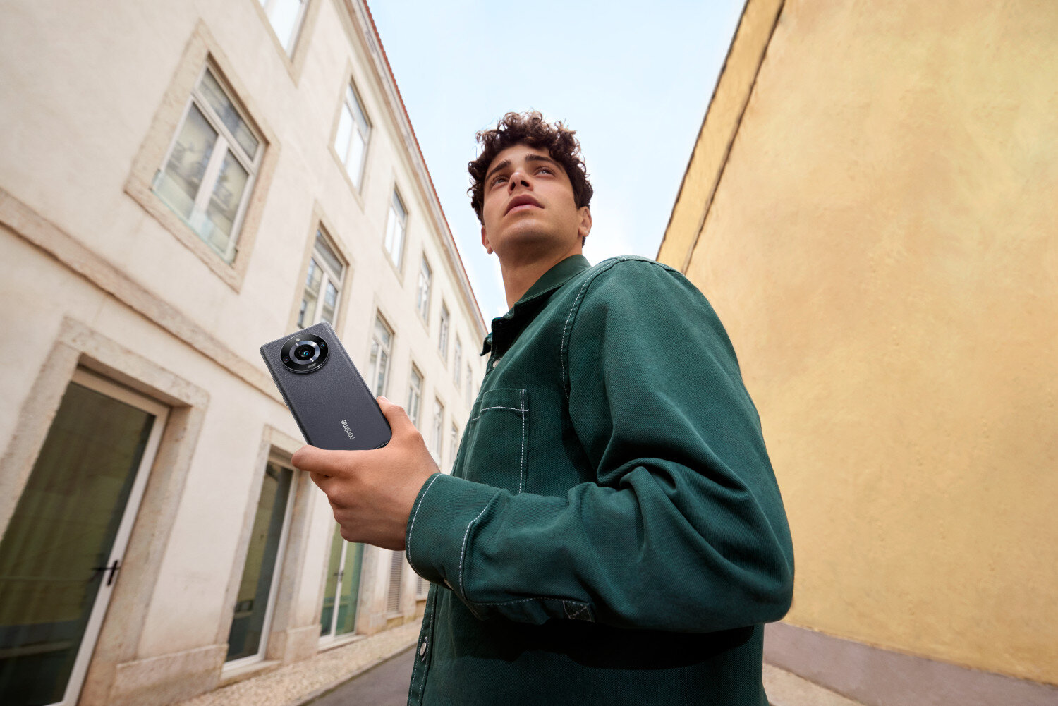 Mężczyzna trzymający czarny smartfon, stojący na ulicy, patrzący w górę.