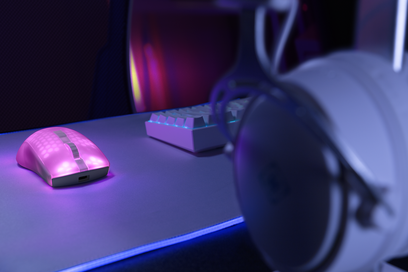 Pinke Gaming-Maus auf einem Schreibtisch mit pinkfarbenem Mauspad. Im Hintergrund Tastatur und Headset.
