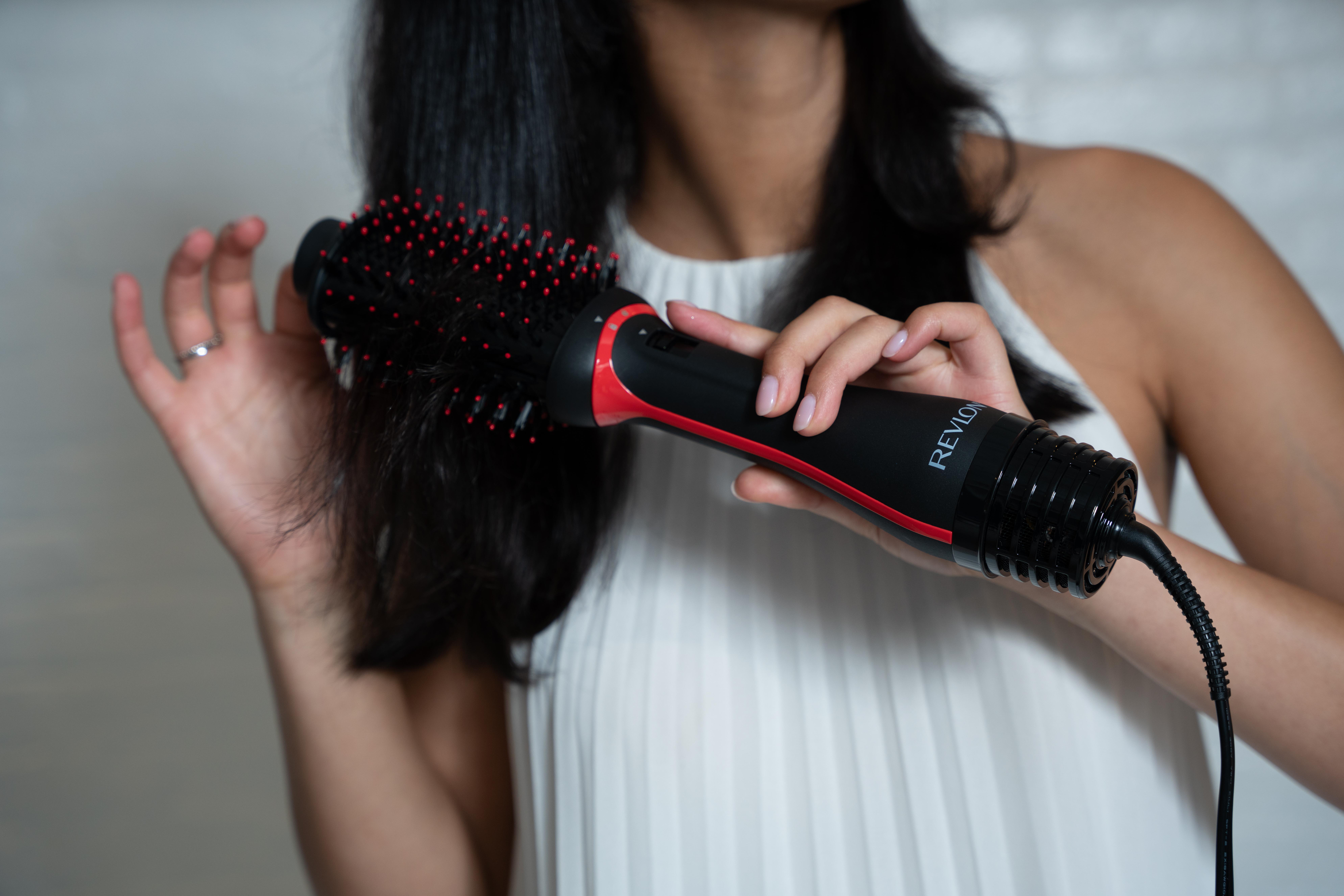 Eine Person, die ihre Haare mit einer rot-schwarzen Revlon-Bürste bürstet.