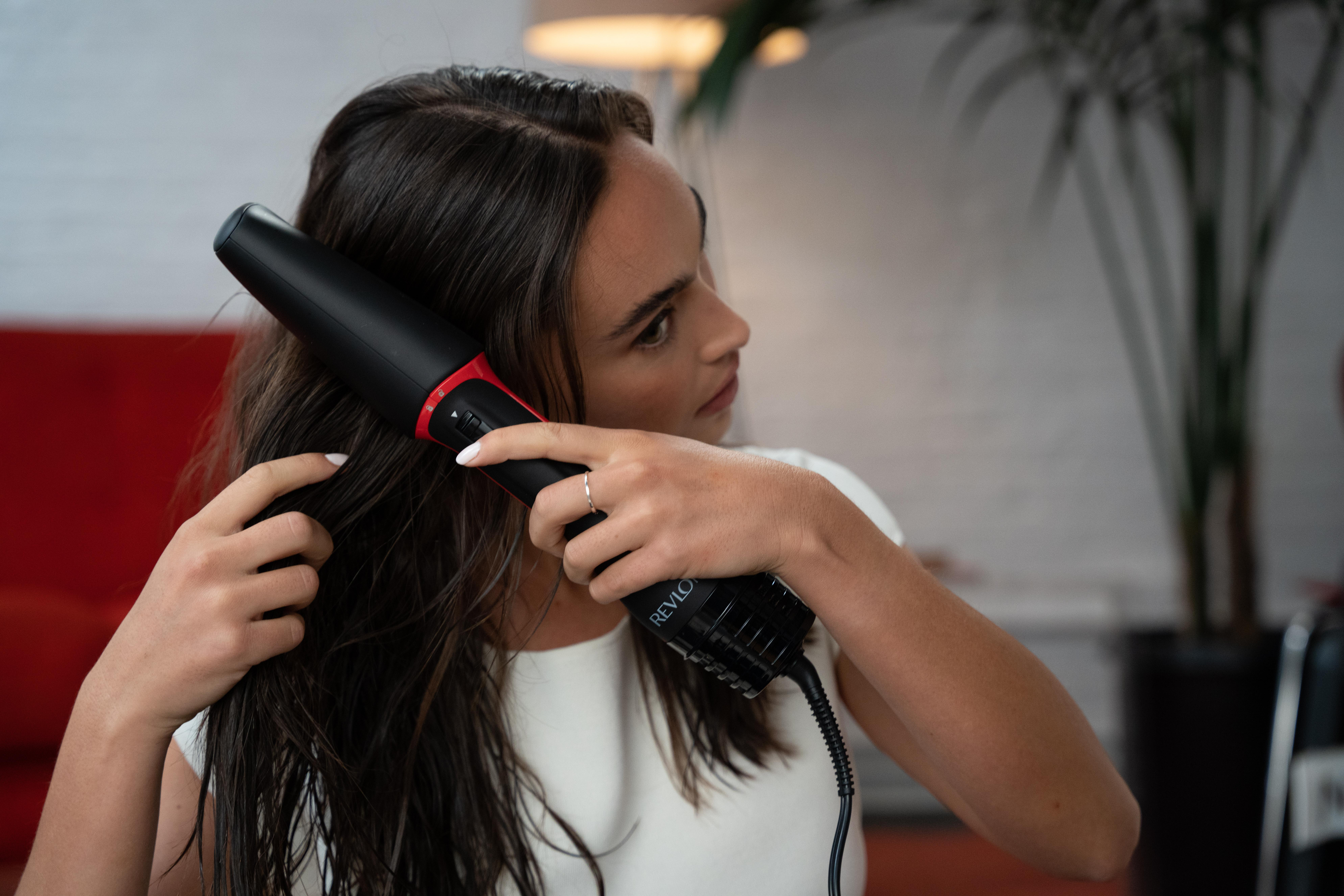 Eine Frau benutzt einen schwarz-roten Haartrockner mit braunen Haaren.