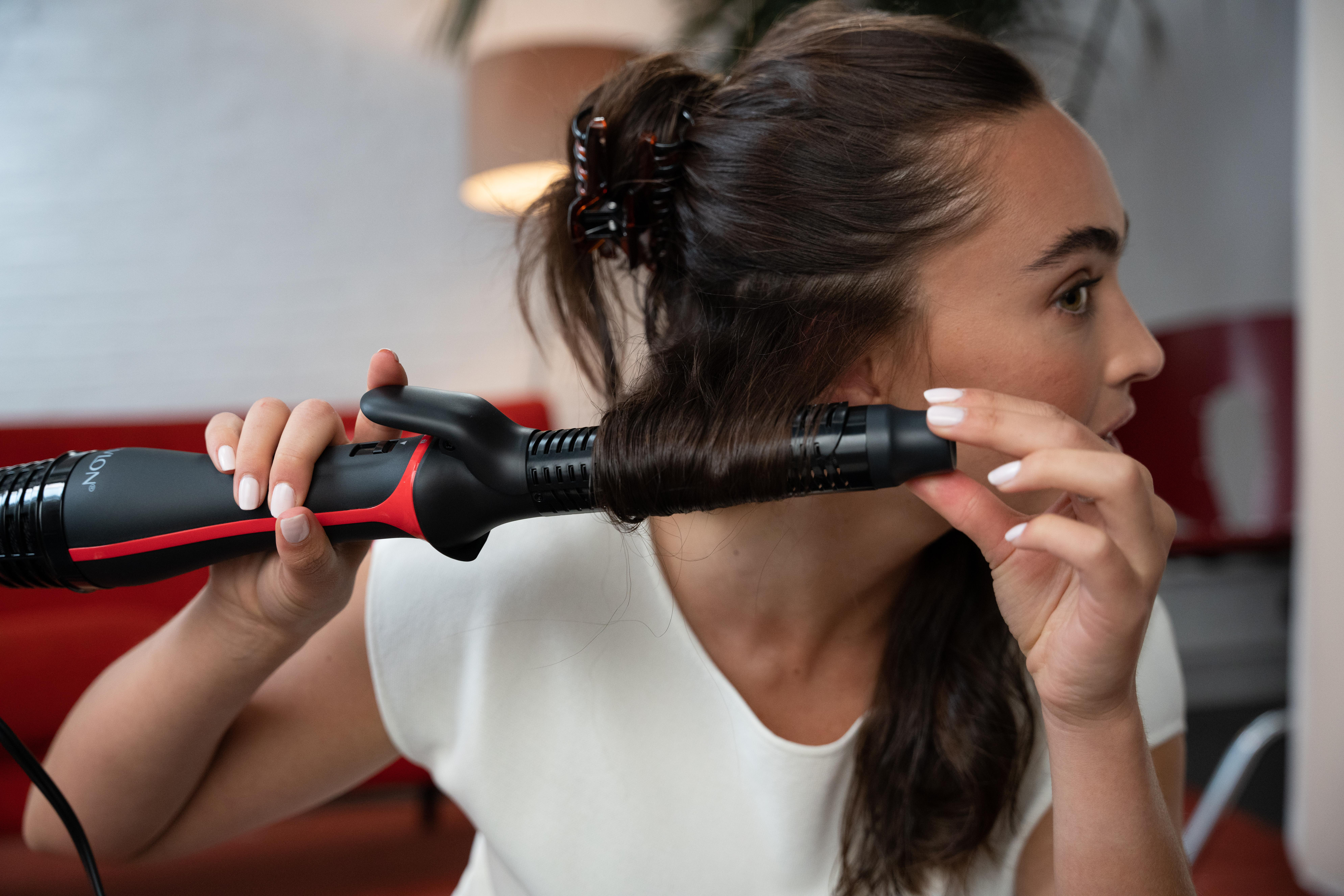Frau, die ihre Haare mit einem schwarzen und roten Revlon-Haarstyler lockt.