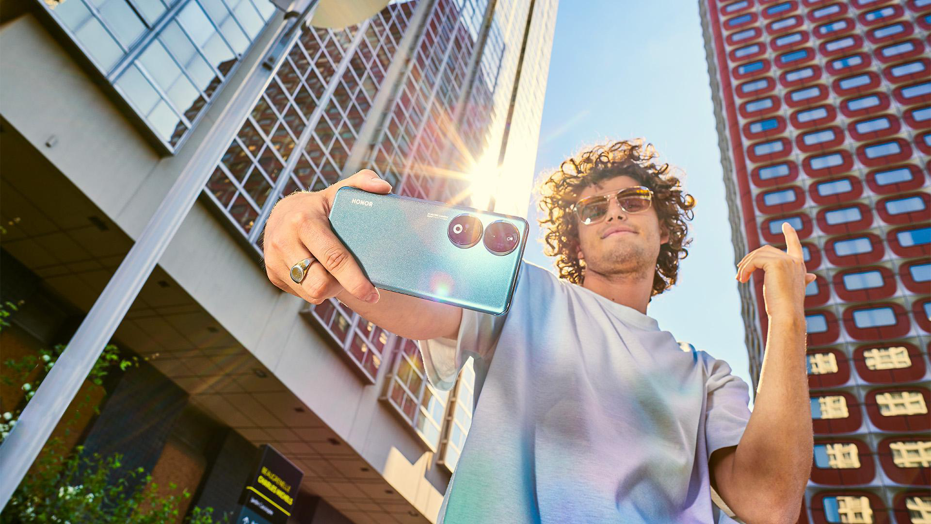 Mann macht Selfie mit türkisfarbenem Telefon vor einem Gebäude.