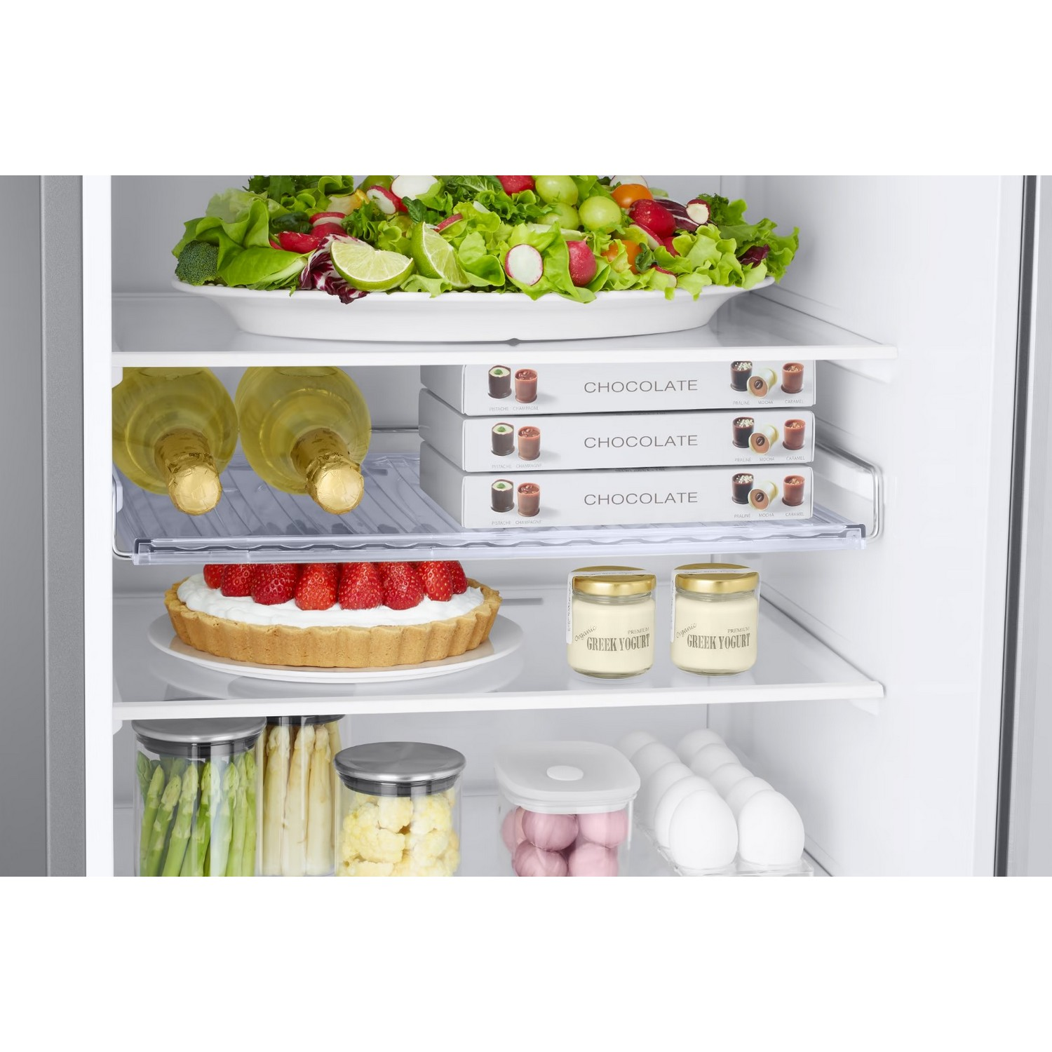 Intérieur du réfrigérateur. Salade, chocolats, vin, tarte, yaourt, asperges et œufs sont visibles.