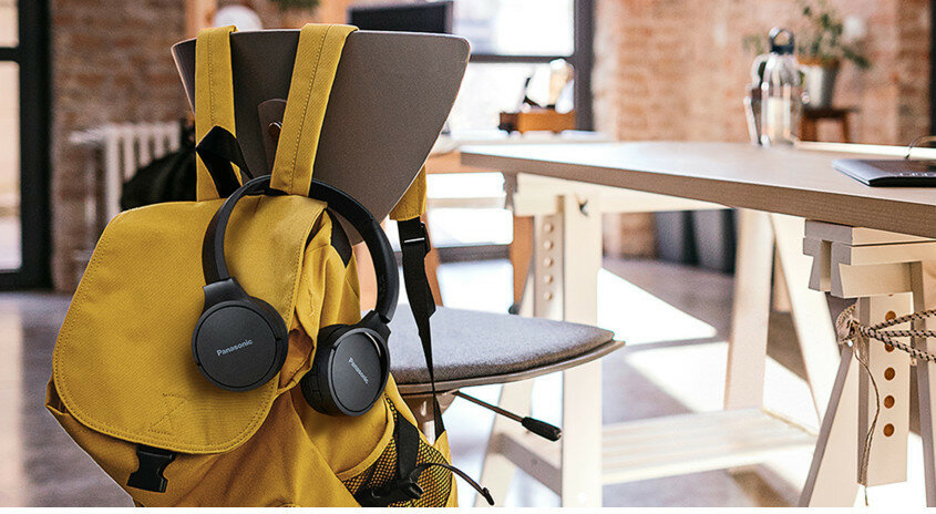 Żółty plecak z czarnymi słuchawkami wiszącymi z boku, w pokoju z biurkiem.