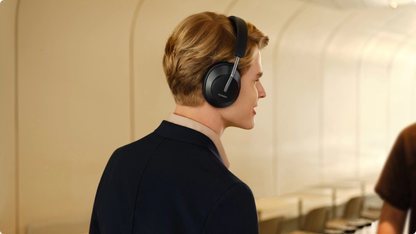 Mężczyzna w czarnych słuchawkach. Ma na sobie czarny garnitur i jasnobrązową koszulę.