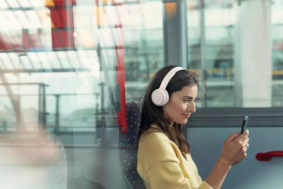 Kobieta w białych słuchawkach, patrząca na smartfona w autobusie.