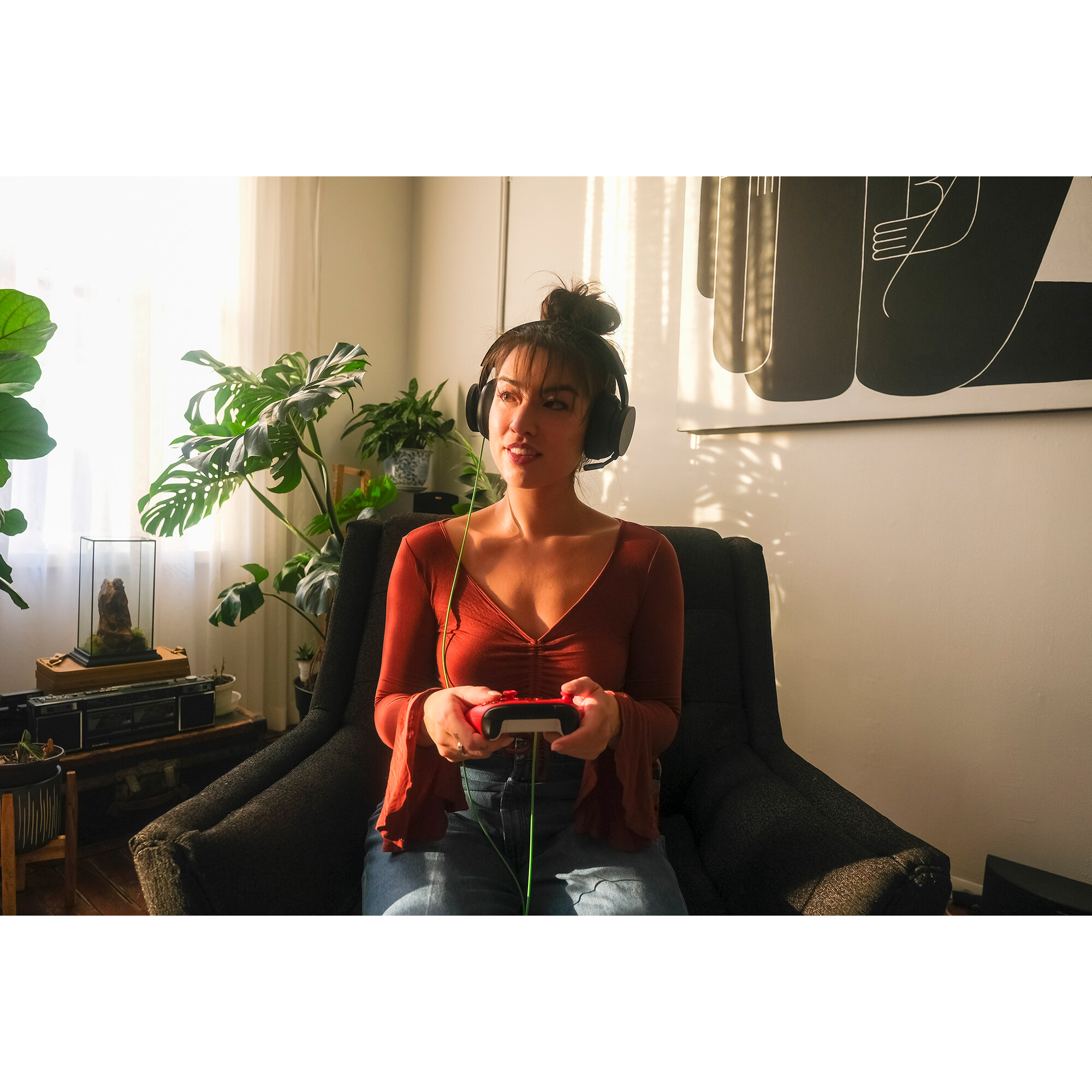 Kobieta w słuchawkach gra w grę wideo. Rośliny i dzieła sztuki w tle.