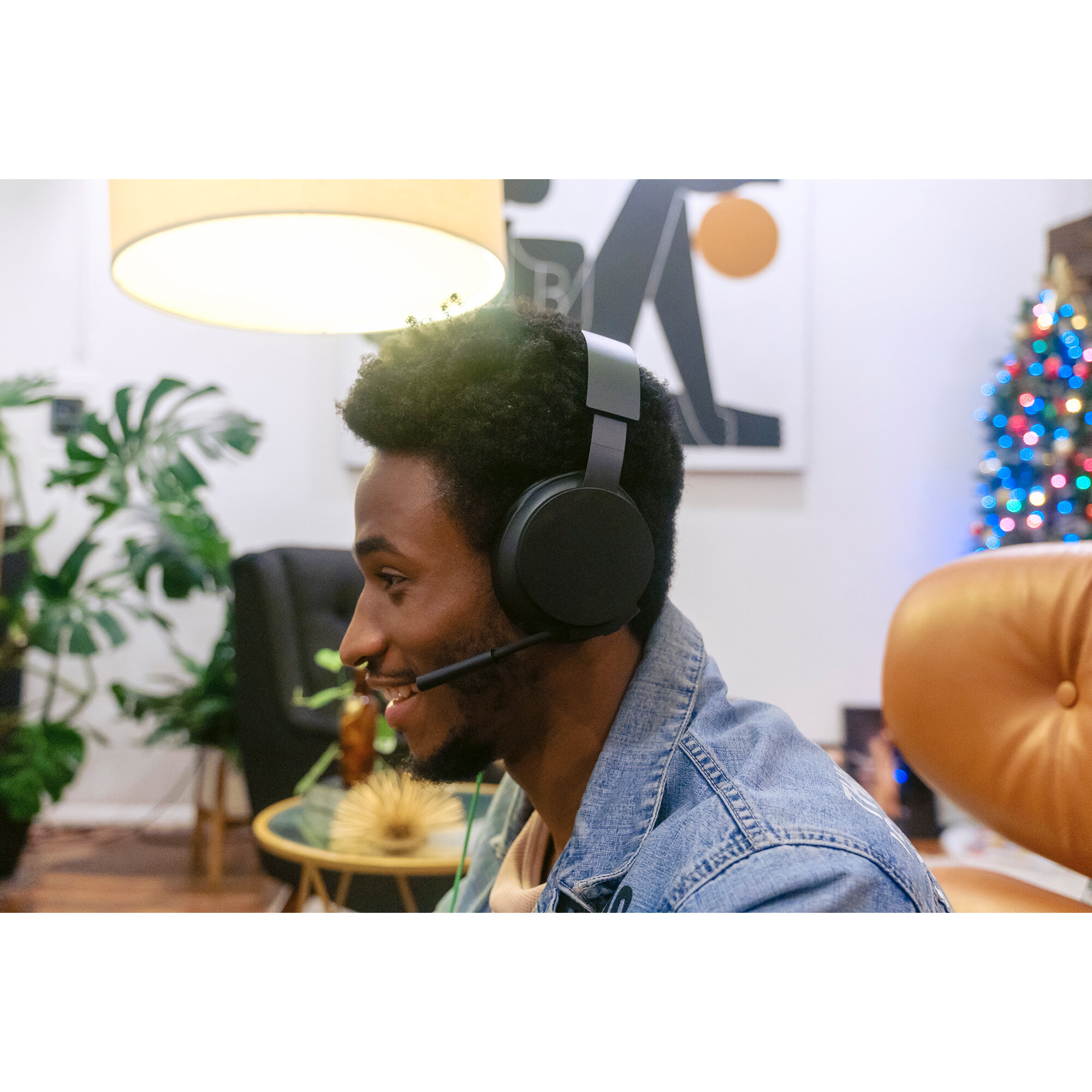 Mężczyzna w czarnych słuchawkach z mikrofonem. Uśmiecha się, w pokoju z drzewem.