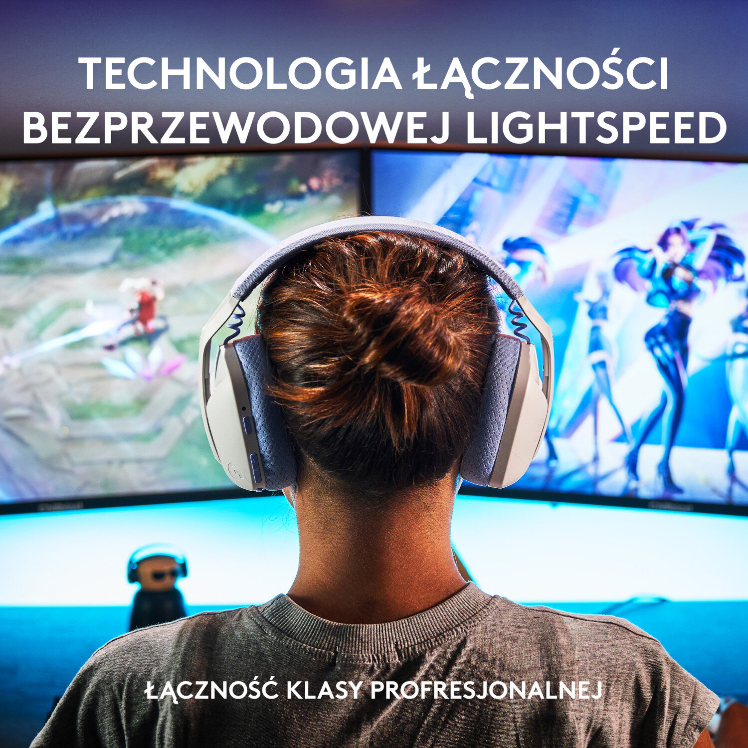 Osoba nosząca białe i szare słuchawki widziana od tyłu. Widoczne dwa ekrany.