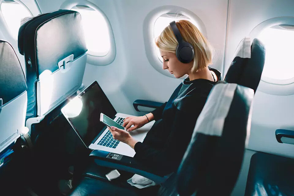Kobieta w samolocie korzystająca z laptopa i telefonu, nosząca słuchawki.