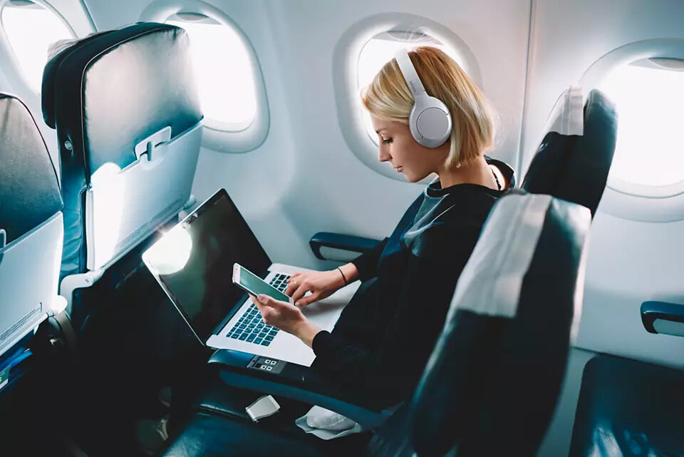 Kobieta w samolocie z laptopem i telefonem, w białych słuchawkach.