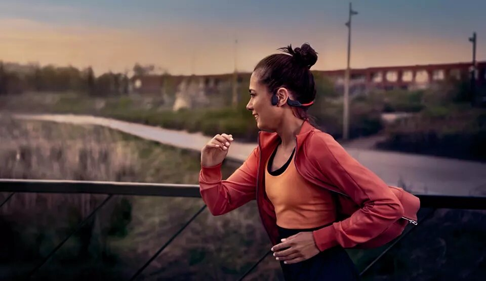 Kobieta biegnąca w słuchawkach kostnych po moście.