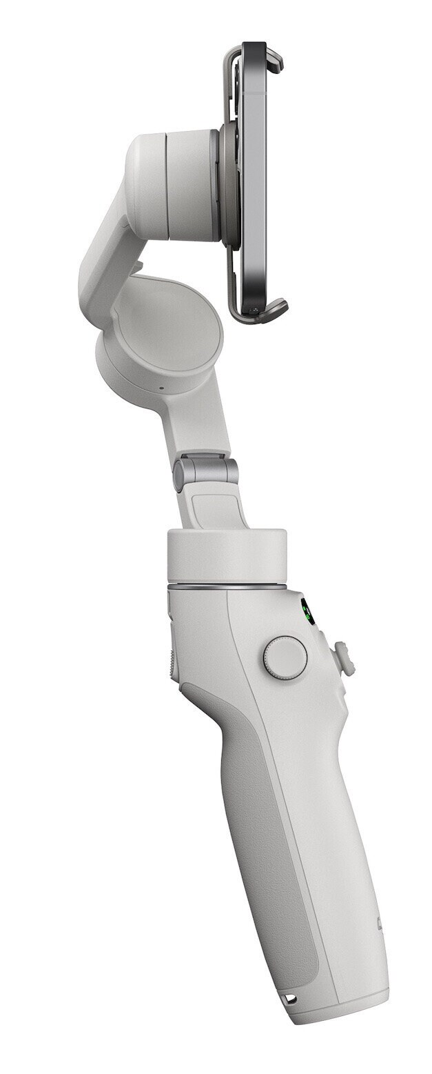 Biały stabilizator ręczny z przymocowanym czarnym telefonem. Jest trzymany pod kątem, gotowy do nagrywania.