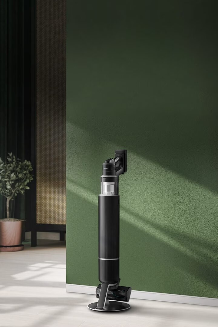 Czarny odkurzacz na uchwycie ściennym, na tle zielonej ściany.