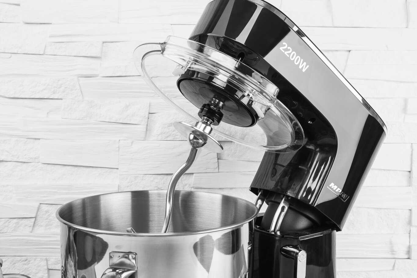 Czarny mikser stojący z hakiem w stalowej misie, na tle białej teksturowanej ściany.