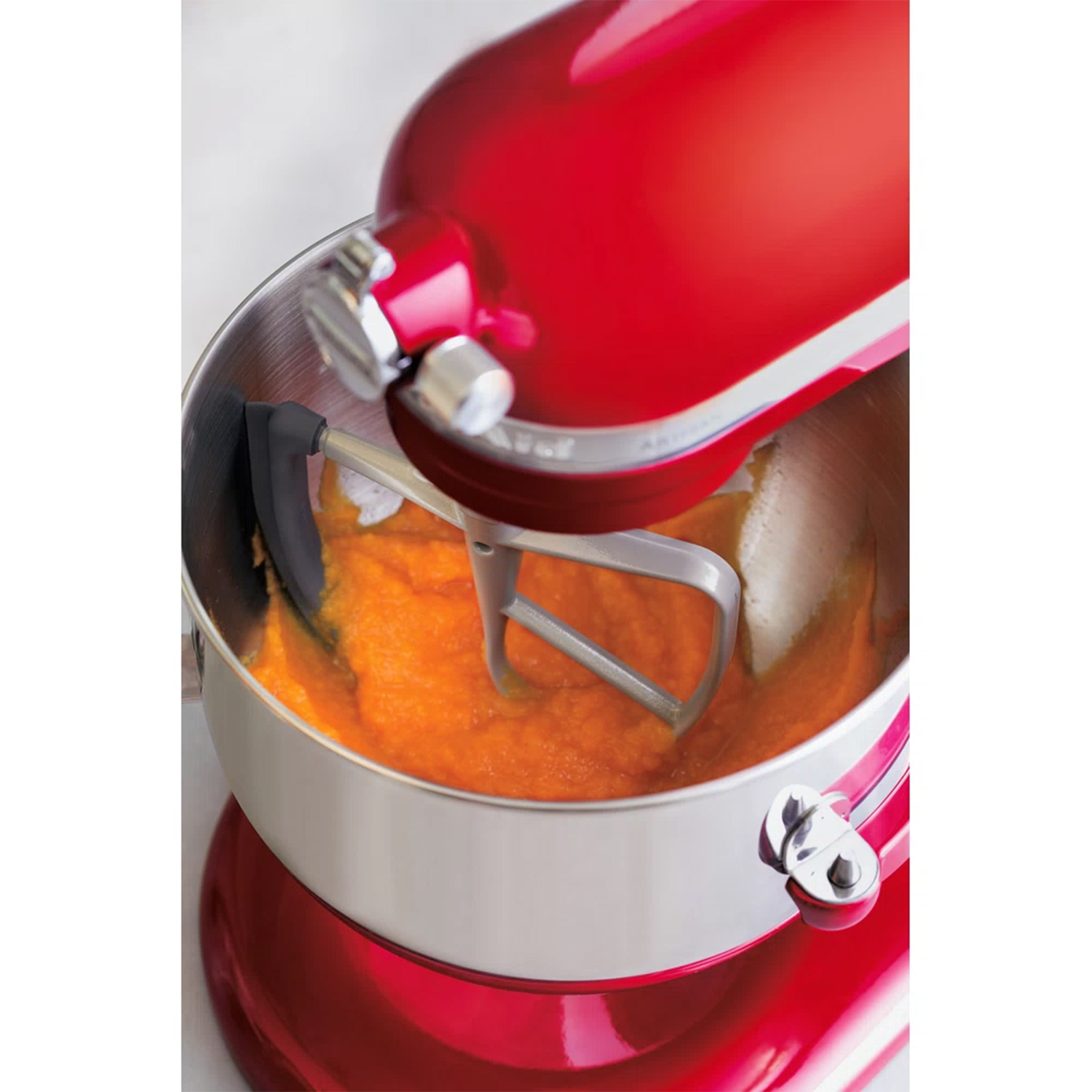Frullatore KitchenAid rosso con ciotola d'argento. Il cibo arancione viene mescolato nella ciotola.