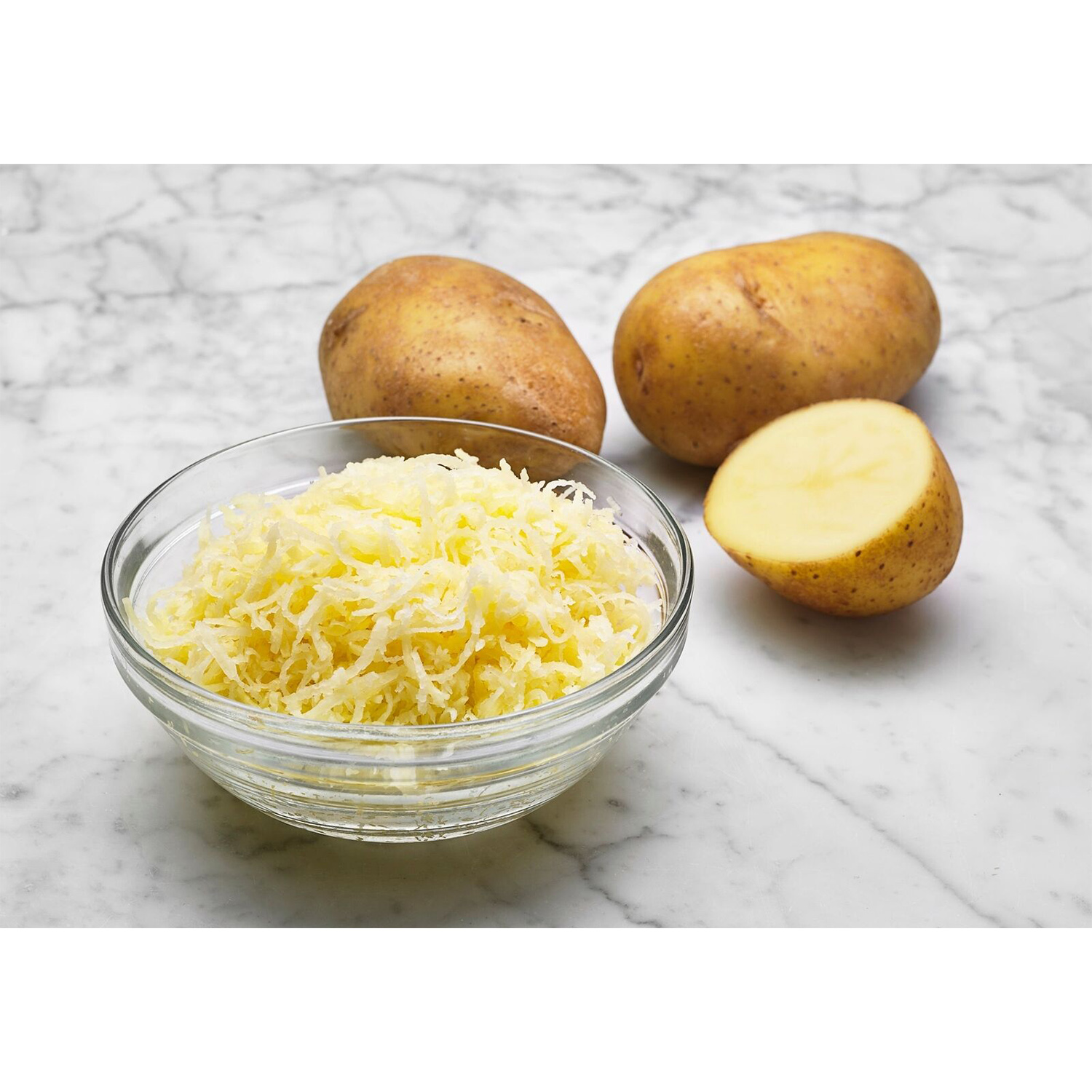 Patate grattugiate in una ciotola di vetro. Due patate intere e mezza.