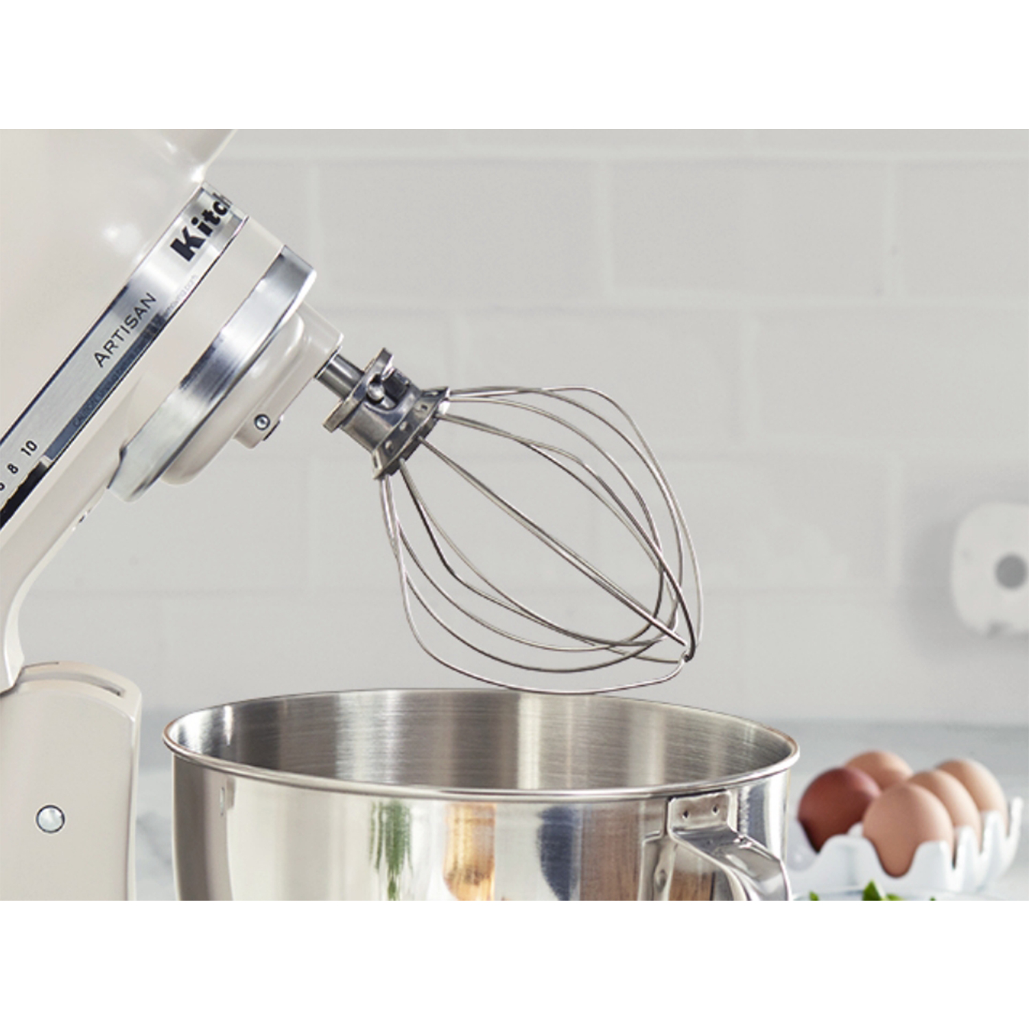Un mixer KitchenAid bianco con accessorio frusta, una ciotola e un vassoio di uova.