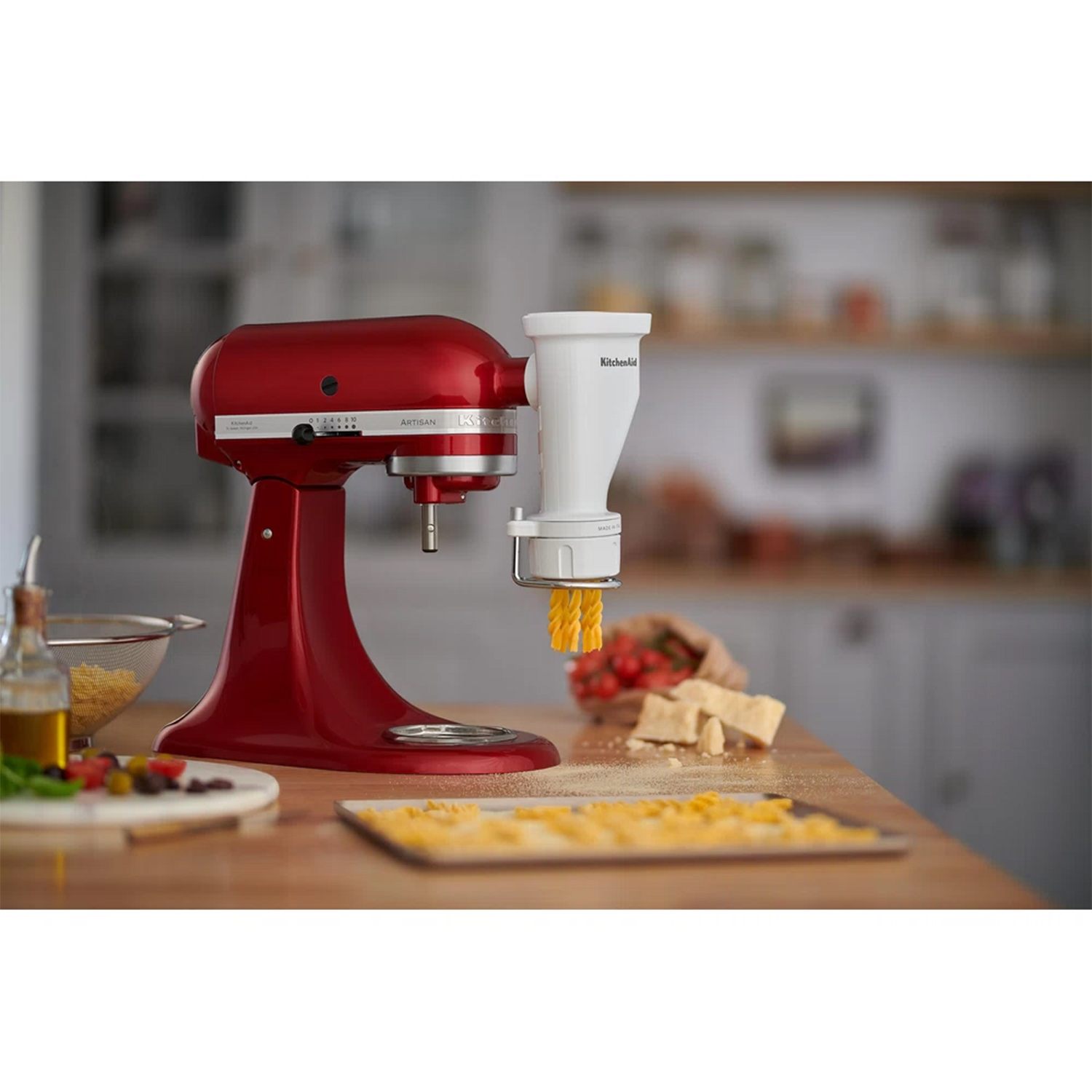 Frullatore KitchenAid rosso con accessorio per pasta. Pasta fatta su tavolo legno.