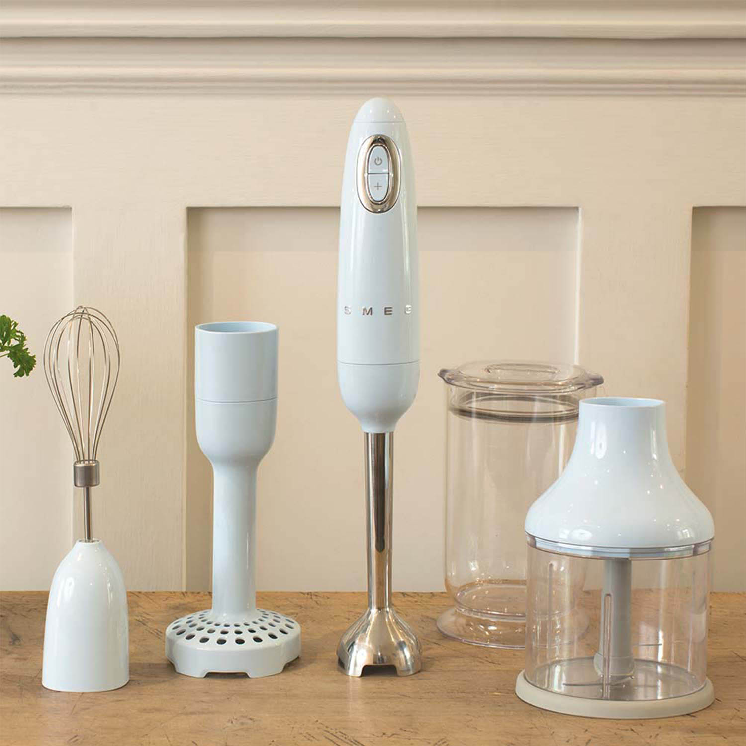Set frullatore a immersione con accessori: frusta, albero di miscelazione e bicchiere. Sfondo chiaro.