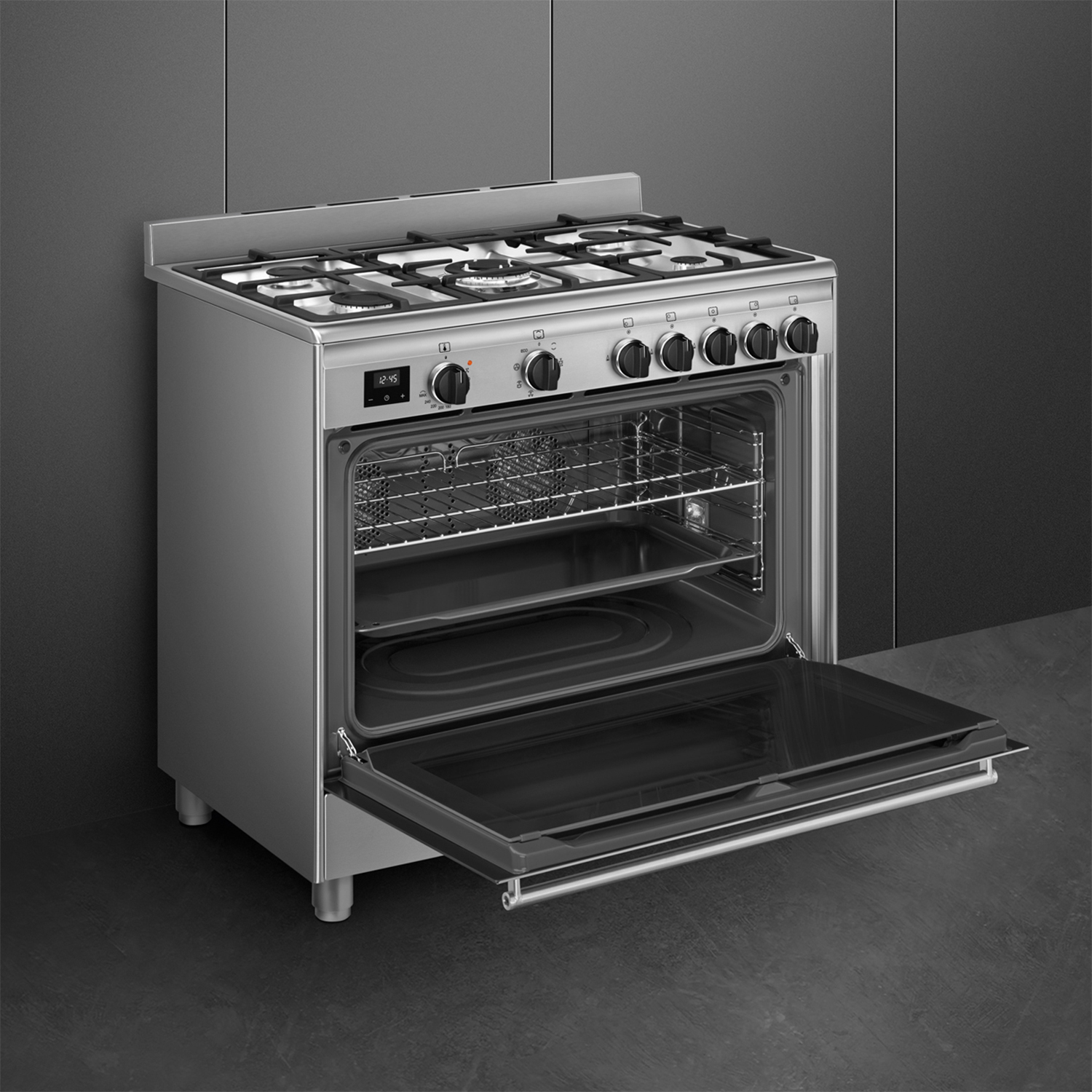 Forno in acciaio inox con porta aperta. Interno visibile con ripiani. Contro un muro grigio scuro.