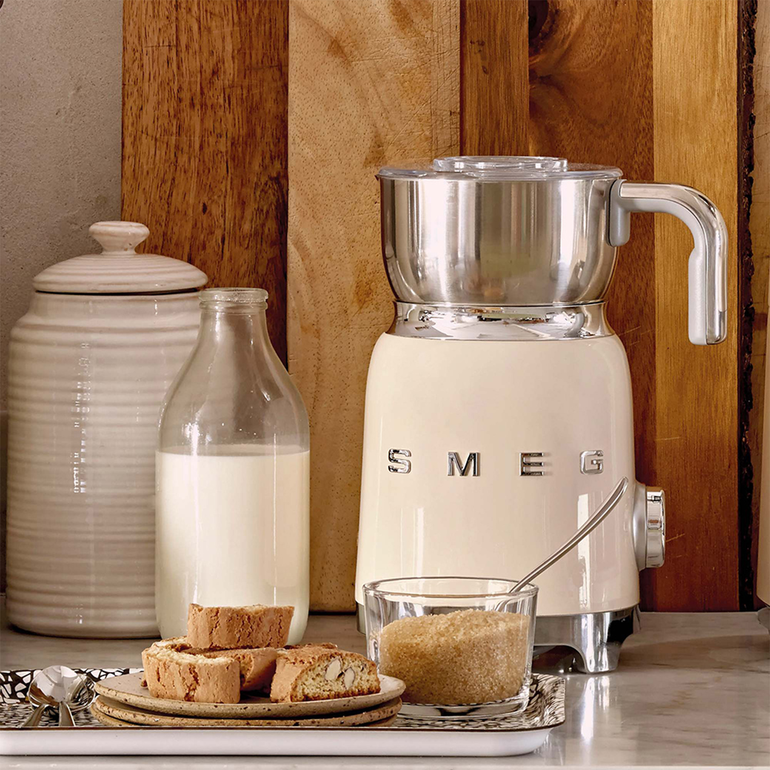 Elettrodomestico da cucina color crema con bottiglia di latte, biscotti e zucchero. È un robot da cucina.