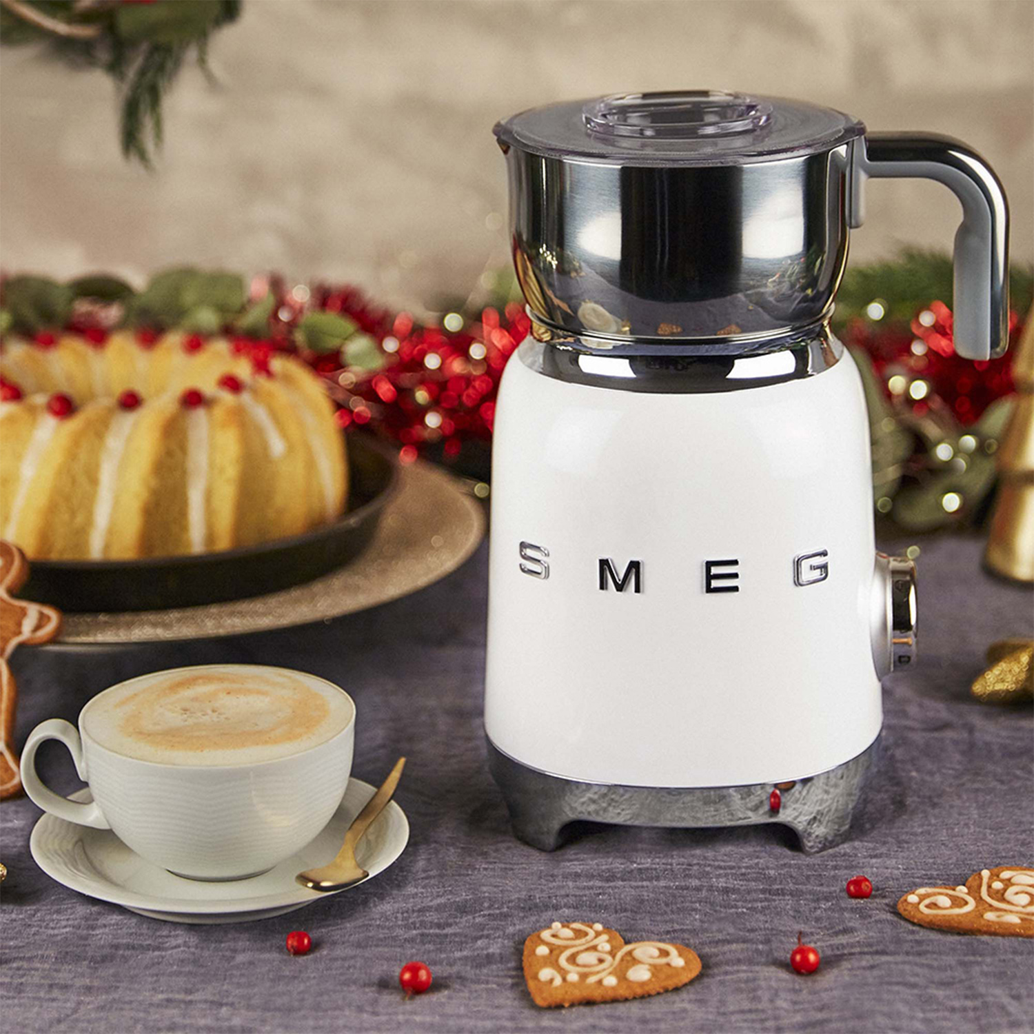 Una macchina da caffè Smeg bianca con una tazza di caffè, una torta e biscotti su un tavolo. Decorazioni natalizie.