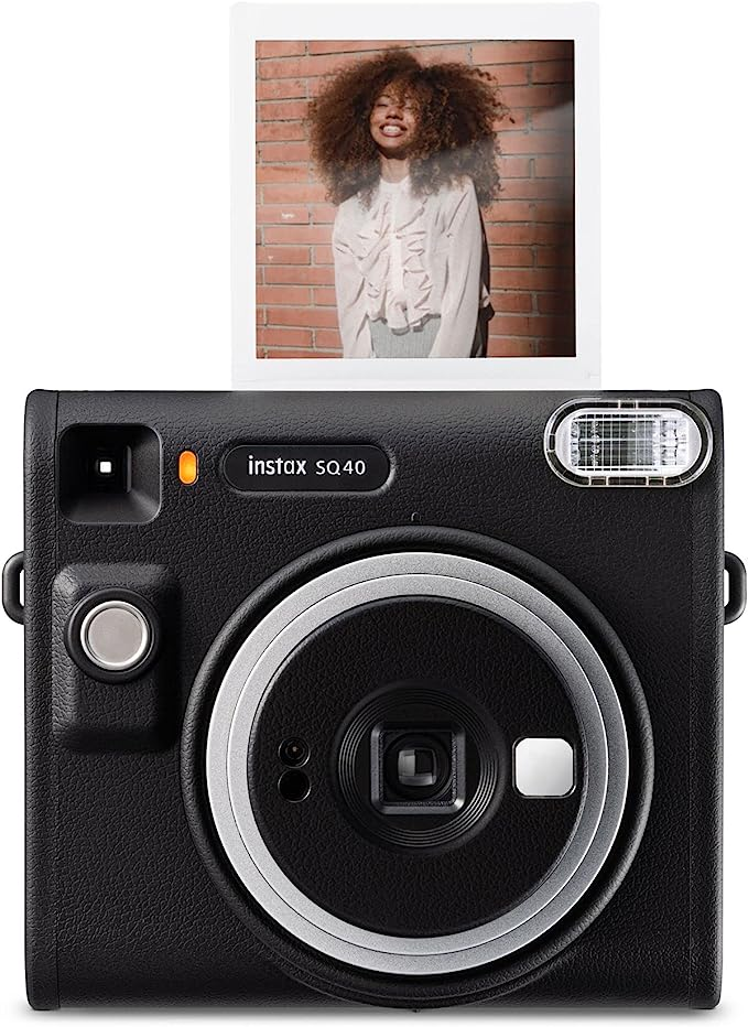 Cámara Instax SQ40 negra con foto de mujer sonriendo, contra pared de ladrillos.