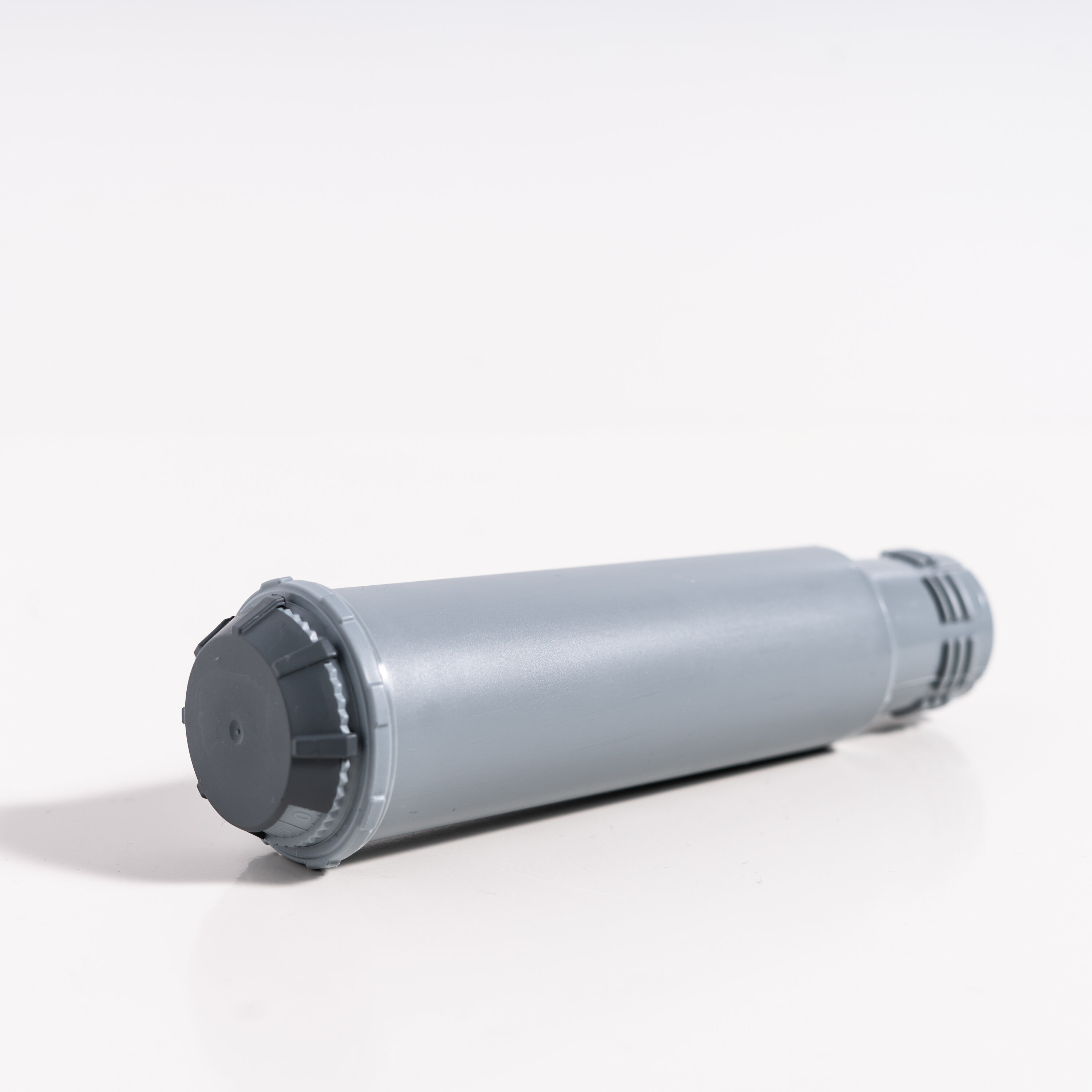 Szary plastikowy cylinder z nakrętką na jednym końcu. Leży na białej powierzchni.