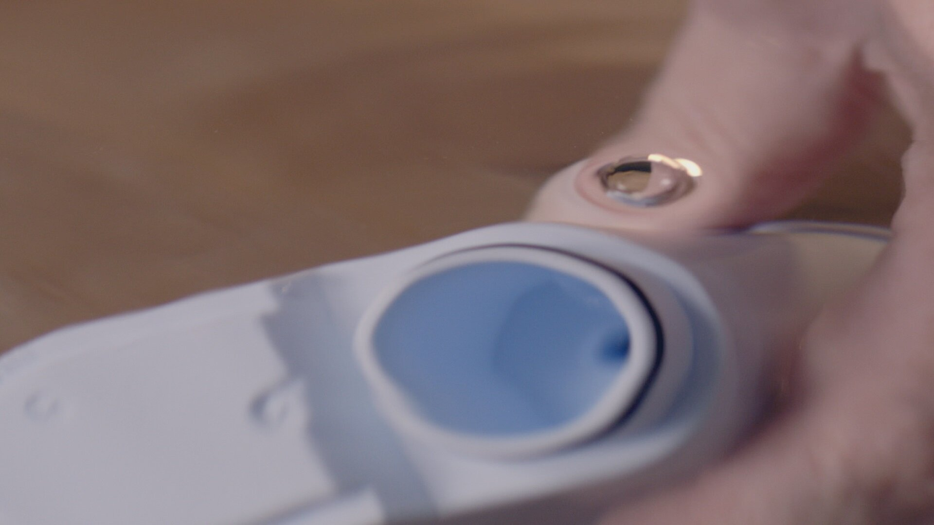 Dłoń trzymająca biało-niebieski element maszyny z niebieskim otworem.