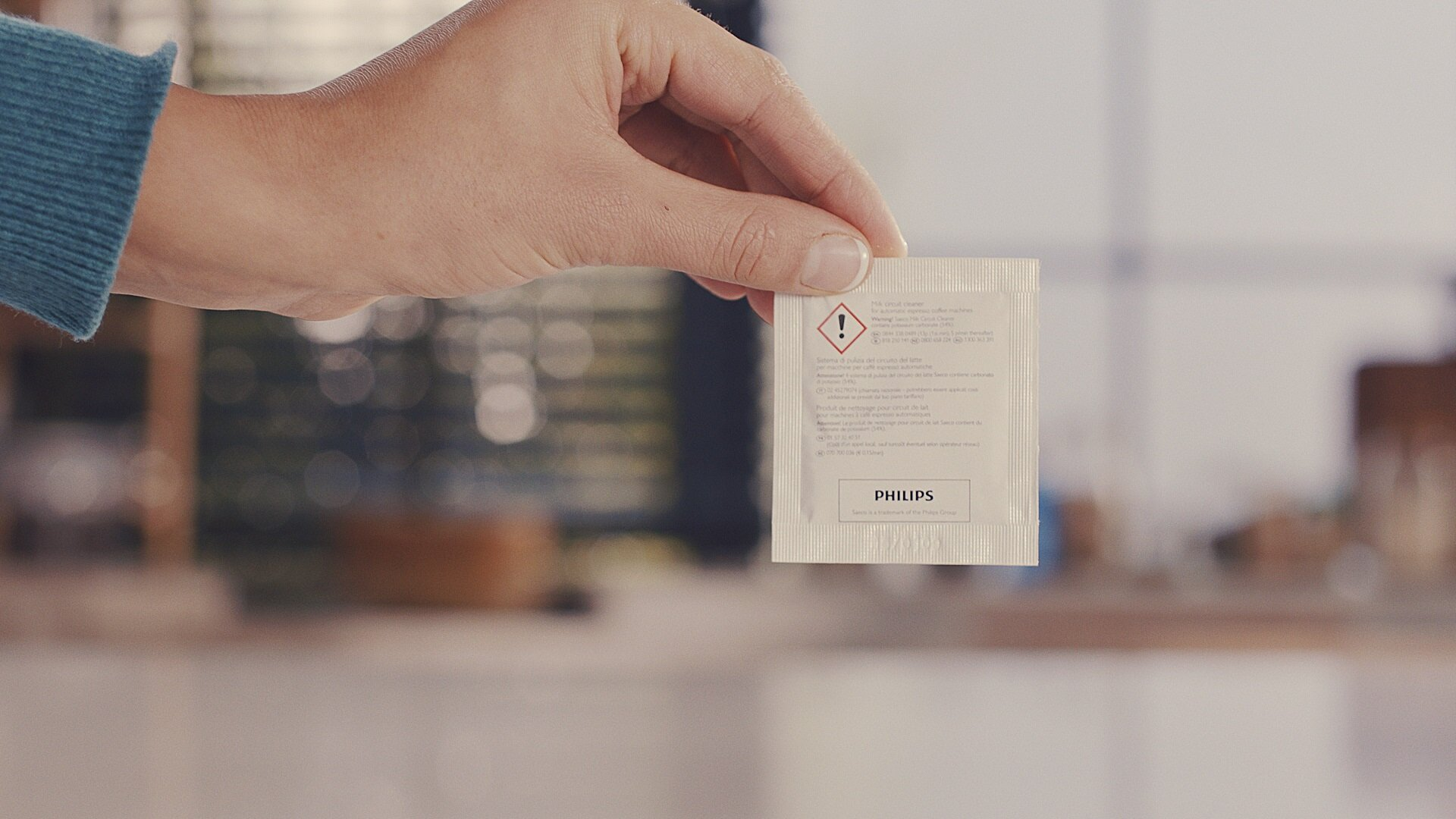 Ręka trzymająca opakowanie Philips z tekstem i logo. Tło to rozmyta scena kuchenna.