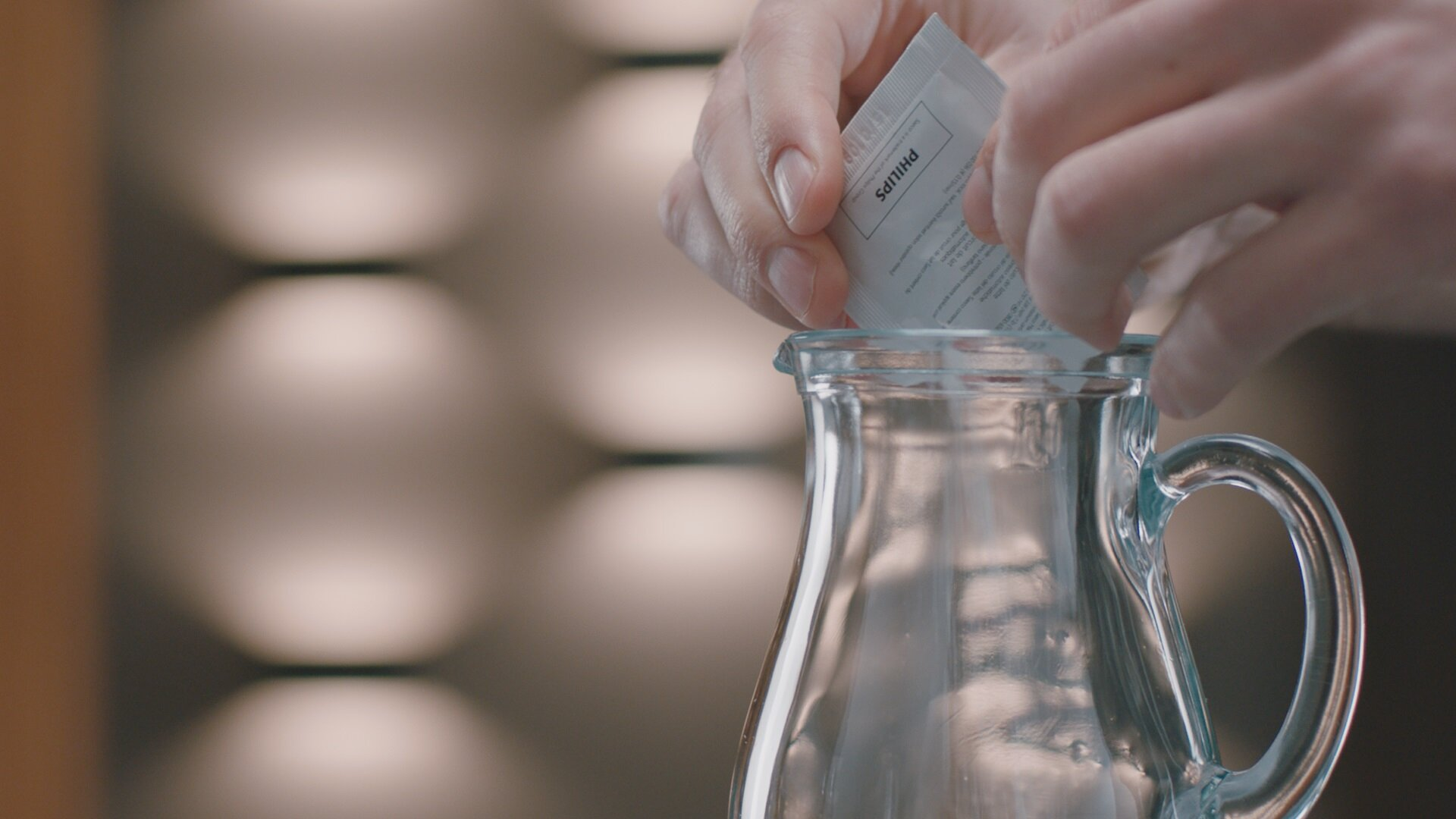 Osoba otwiera opakowanie filtra wody Philips i wlewa zawartość do szklanego dzbanka.