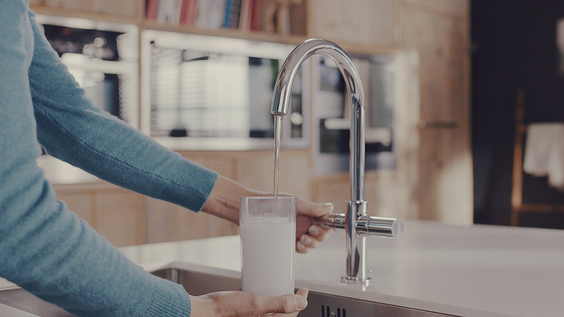 Osoba nalewa wodę z kranu do przezroczystego szkła. Szklanka jest w połowie pełna.
