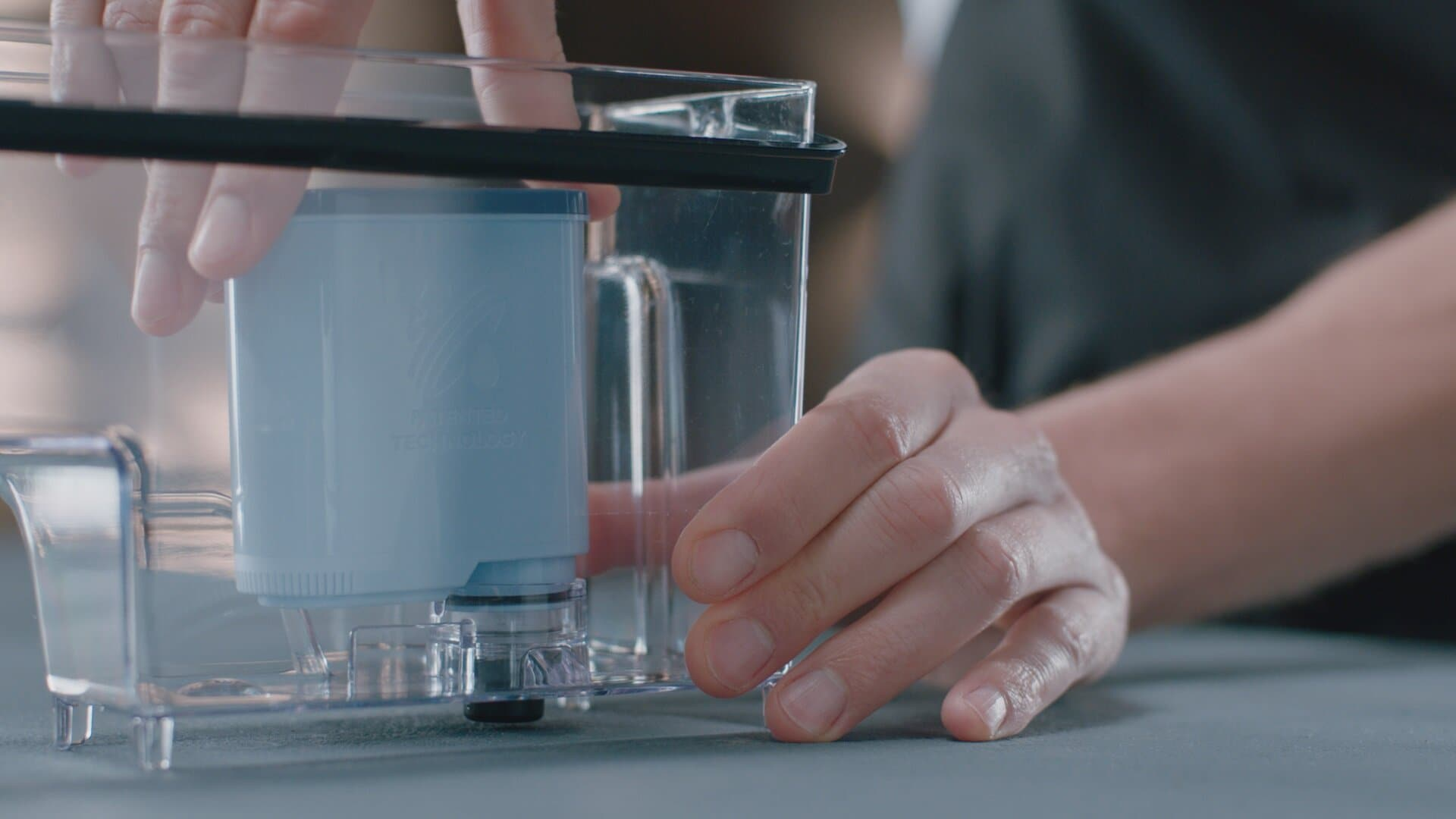 Ręce osoby montującej filtr wody. Niebieski filtr jest umieszczany w przezroczystym pojemniku.