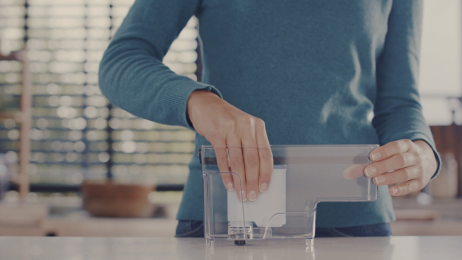 Dłonie kobiety umieszczające filtr w przezroczystym zbiorniku na wodę.