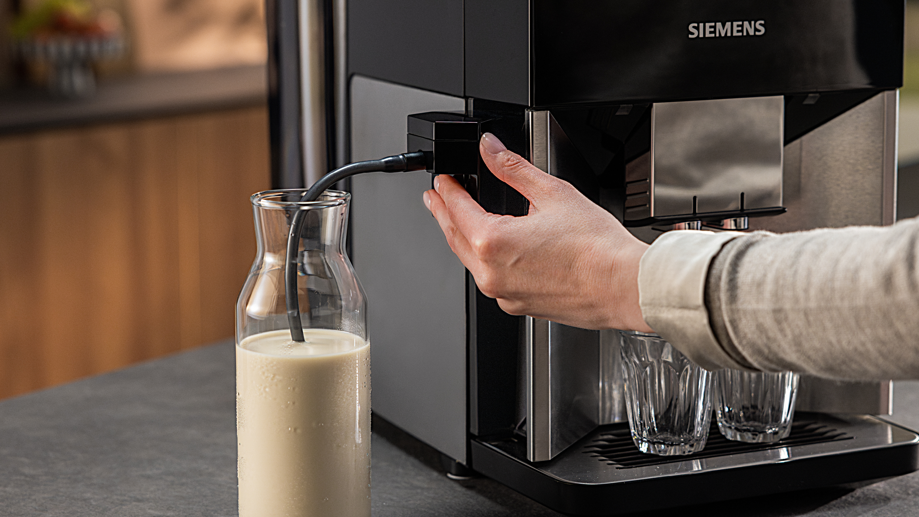Person benutzt eine Kaffeemaschine. Milch in eine Glasflasche gießen. Die Maschine ist schwarz und silber.