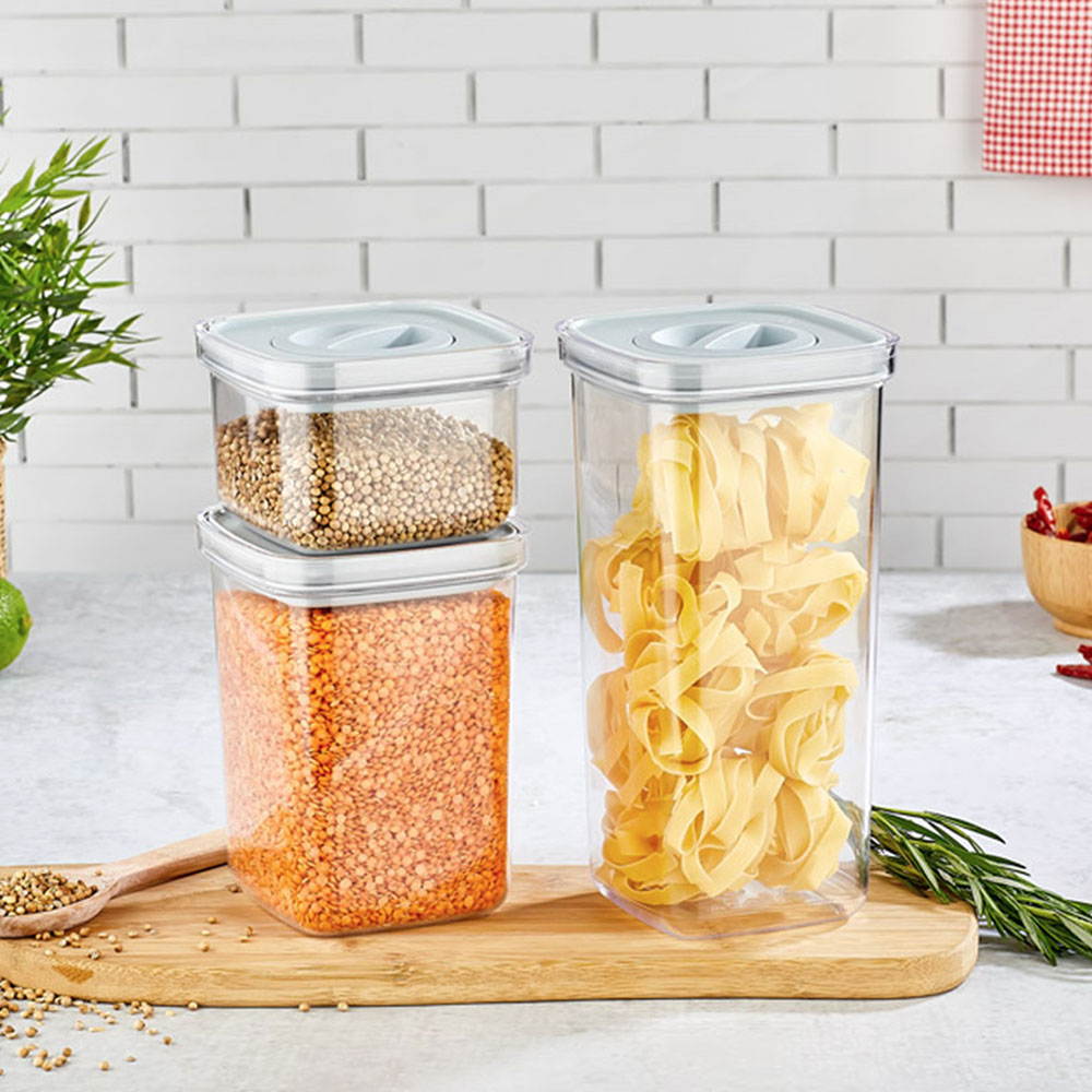 Kapalı şeffaf plastik kaplar, tahta üzerinde mercimek, makarna ve kişniş tohumları ile dolu.
