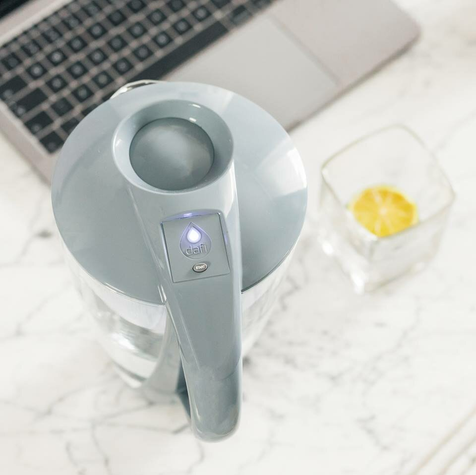 Szary dzbanek filtrujący wodę z uchwytem i szklanka wody z cytryną na marmurowej powierzchni.