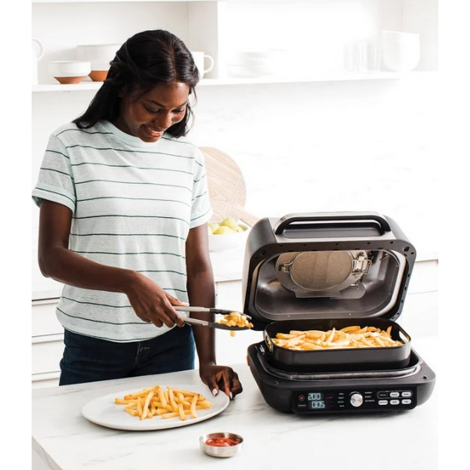 Woman placing fries on a plate. An air fryer and a plate of fries are on the kitchen counter.