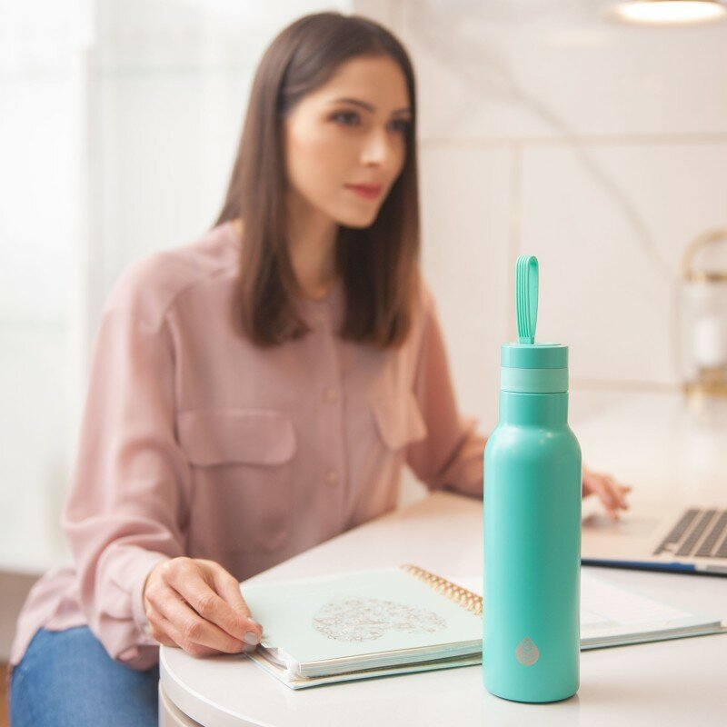 Kobieta w różowej koszuli siedzi przy biurku z turkusową butelką wody.